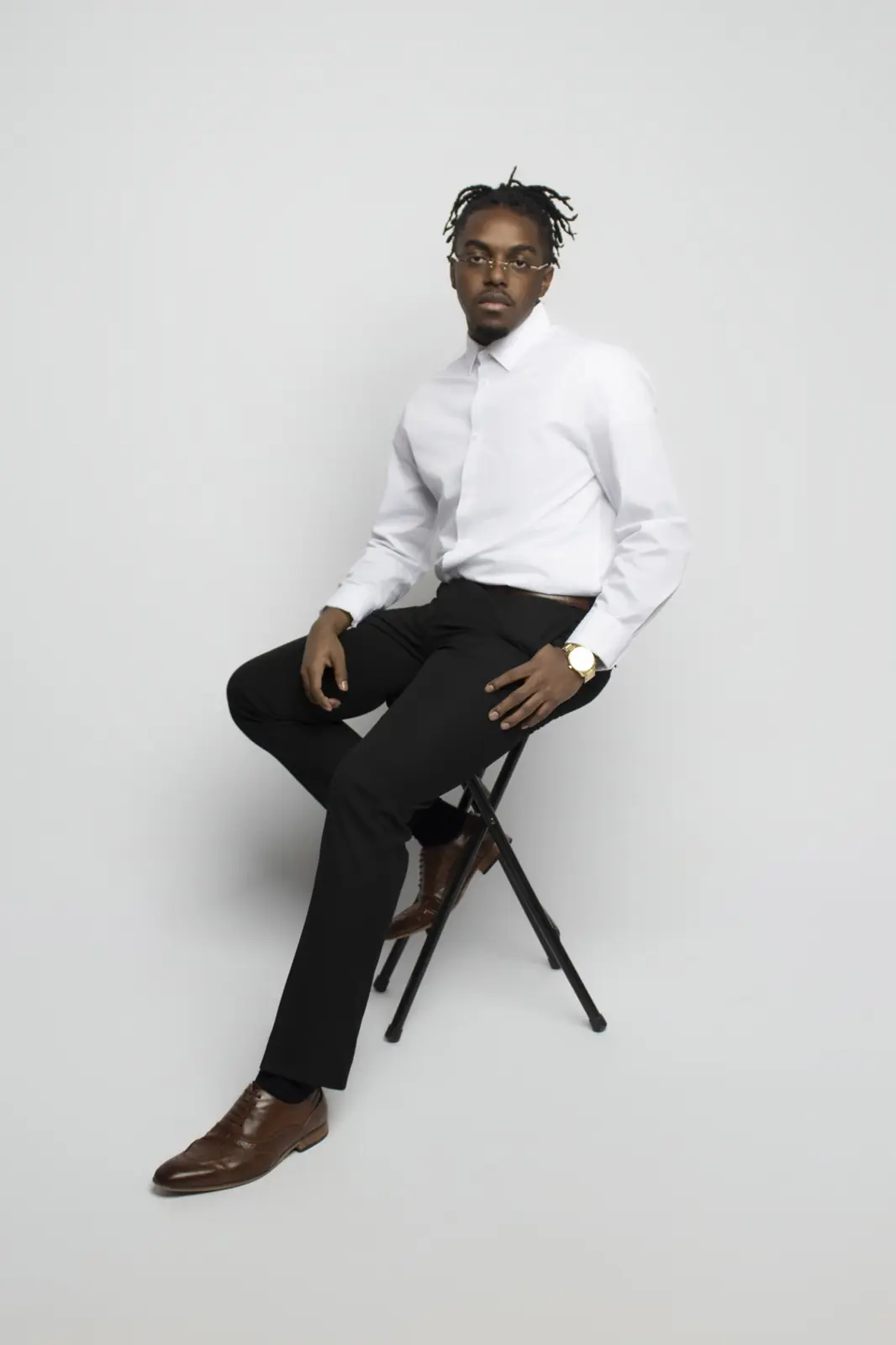 John Murrel seated on a black stool in a white shirt and black trousers